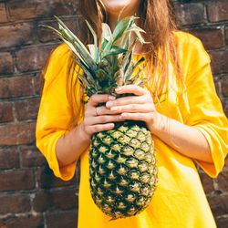 Midsection of woman holding pineapple against wall
