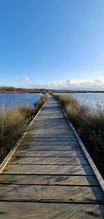 Boardwalk leading towards lake against sky