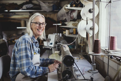 Portrait of smiling owner using sewing machine at workshop