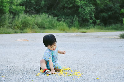 Full length of cute boy playing while siting on road