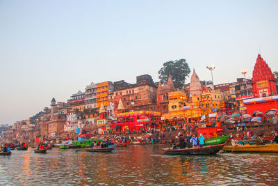 Boats in river by buildings against clear sky