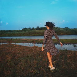 Woman standing on field by lake against sky