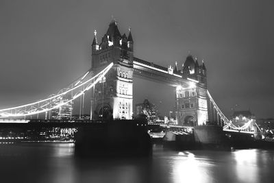 Illuminated bridge over river against sky in city at night