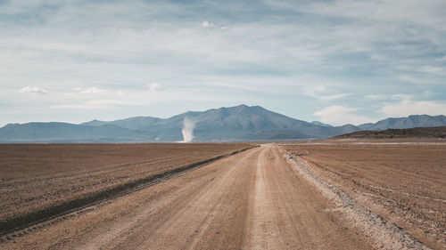 Dirt road passing through desert against sky