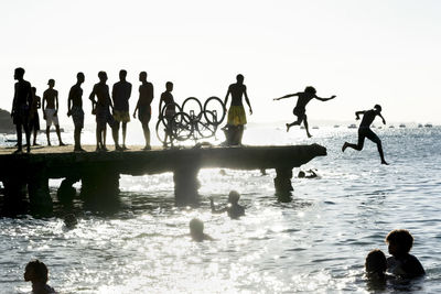 Silhouette of young people jumping from the crush bridge at the yellow sunset .