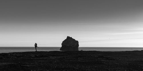 Silhouette man standing on cliff by sea against sky