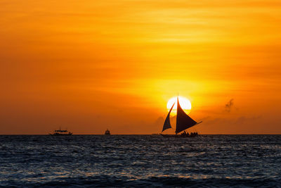 Silhouette sailboat sailing on sea against orange sky