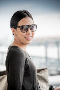 Portrait of smiling young woman in sunglasses against sky