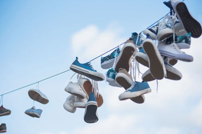 Low angle view of shoes tied on cable against blue sky