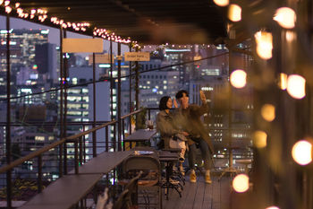 PEOPLE SITTING IN ILLUMINATED MODERN BUILDINGS AT NIGHT