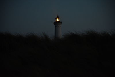 Lighthouse by silhouette building against sky at dusk