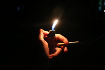 Close-up of human hand holding lighter and cigarette at night