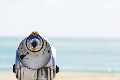 Close-up of coin-operated binoculars by sea against sky