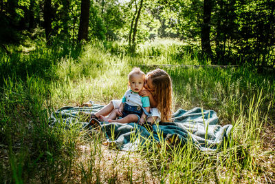 Sister kissing infant brother outside in tall grass