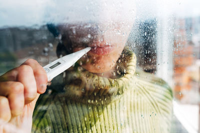 Sick woman checking body temperature near window at home