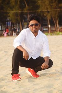 Portrait of young man sitting on sand at beach