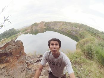 Fish-eye lens view of man looking up while standing against lake on mountain