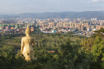 Statue amidst trees and buildings in city against sky