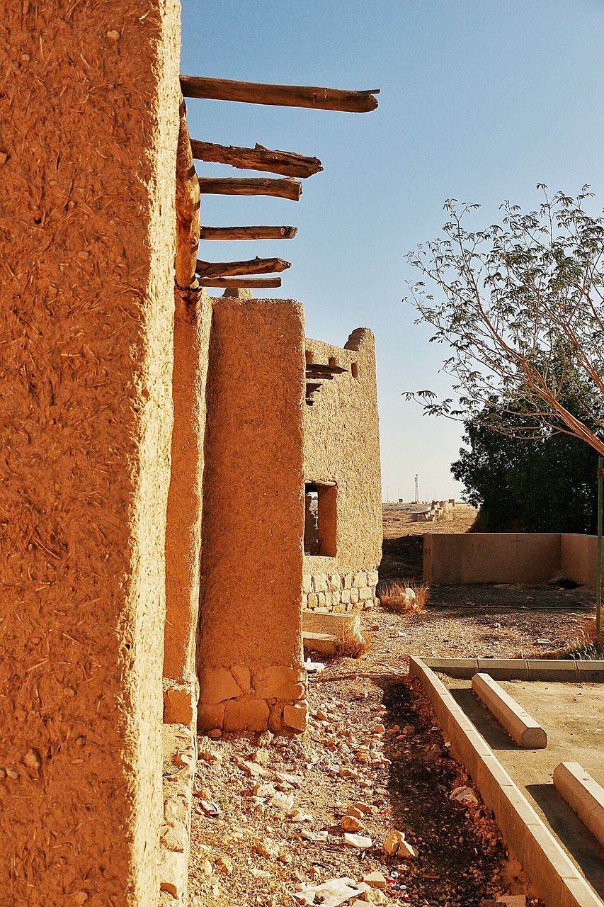 architecture, built structure, building exterior, clear sky, house, sky, roof, residential structure, old, sunlight, outdoors, residential building, abandoned, day, no people, tree, damaged, low angle view, wood - material, shadow