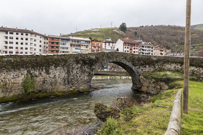 Bridge over river by buildings against sky