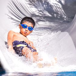 Portrait of shirtless boy in slide at waterpark