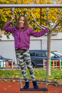 Portrait of girl standing on swing at park