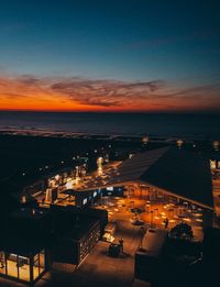 High angle view of illuminated city by sea against sky at sunset