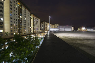 Illuminated street amidst buildings against sky at night