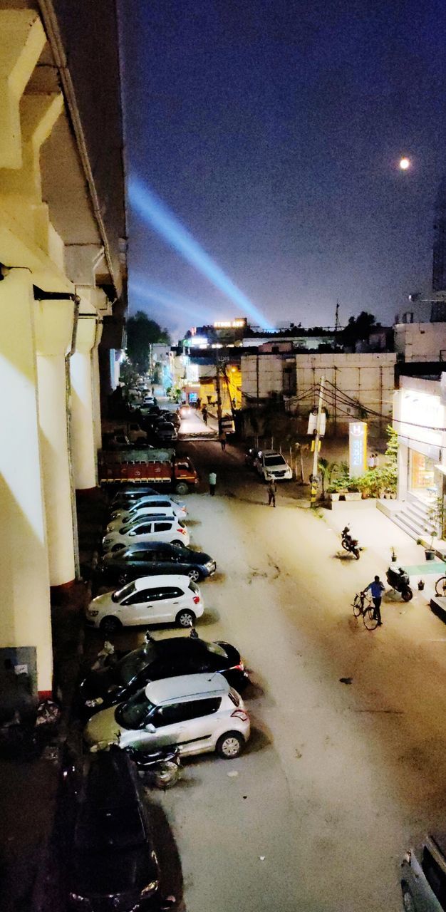 CARS ON ROAD BY ILLUMINATED BUILDINGS AGAINST SKY AT NIGHT