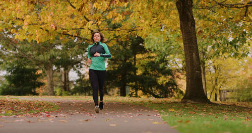 Full length of young woman jogging in park during autumn