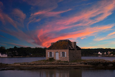 Building by lake against sky during sunset