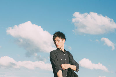 Low angle view of young woman looking away against sky