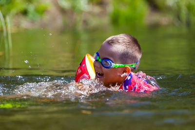 Cute boy is swimming in the small river with his armbands and goggles