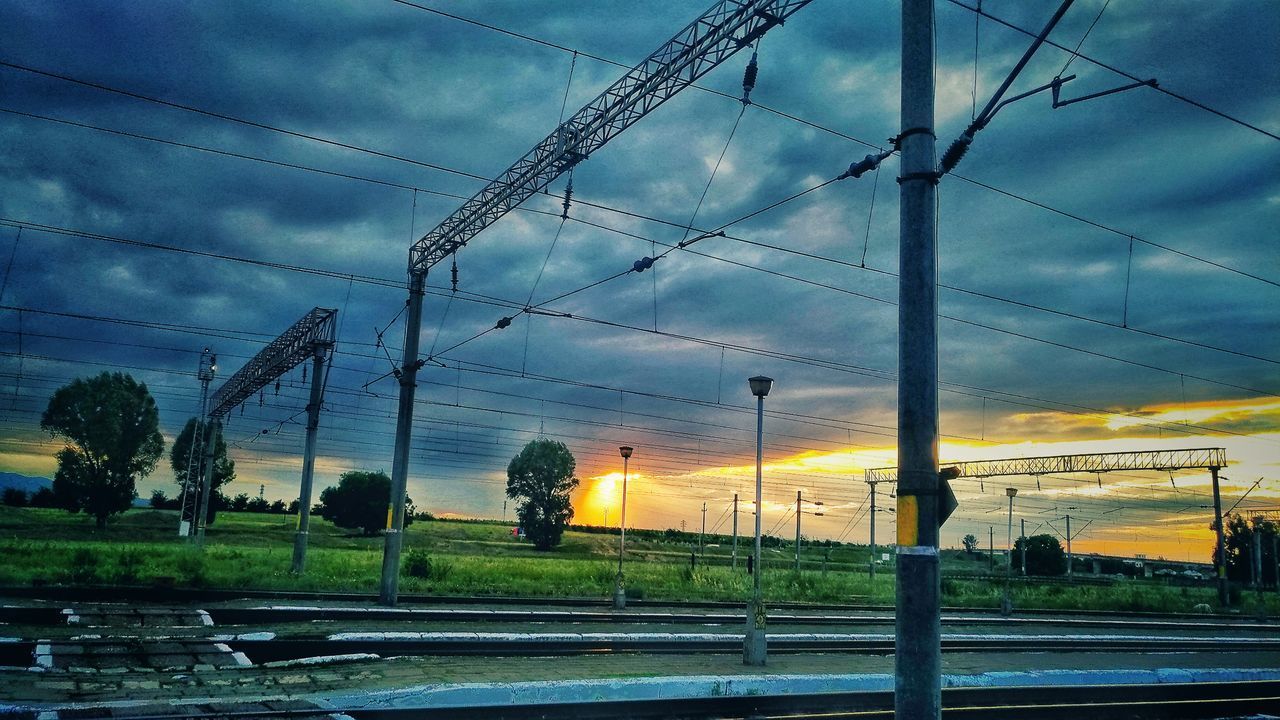 ELECTRICITY PYLONS BY RAILROAD TRACKS AGAINST SKY DURING SUNSET