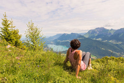 Rear view of woman relaxing on mountain against cloudy sky