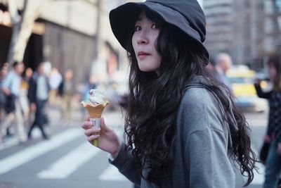 Side view of woman holding ice cream while standing on street in city