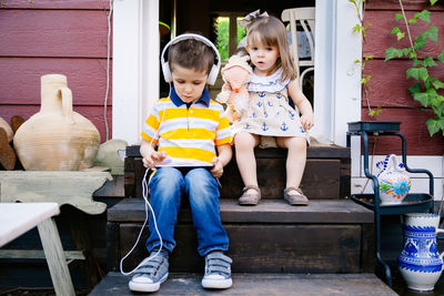 Cute boy listening music with sister at entrance