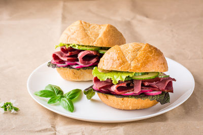 Ready-to-eat hamburgers with pastrami, vegetables and basil on a plate on craft paper