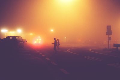 Silhouette people crossing road at night during foggy weather