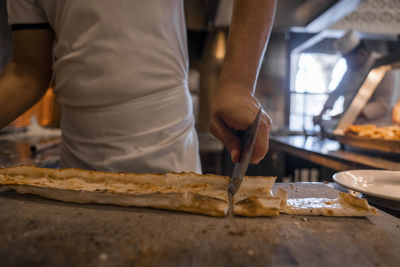 Chef cutting turkish cheese pide into slices on table at restaurant