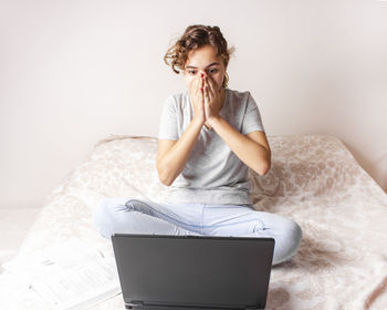 Young woman using mobile phone while sitting on bed