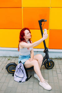 Woman uses a smartphone and an electric scooter in the summer in the city