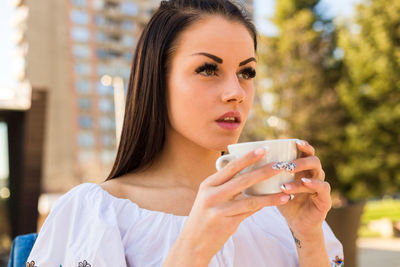 Thoughtful young woman having coffee while sitting at outdoor cafe in city