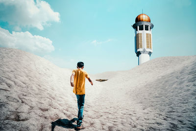 Rear view of boy walking on land against lighthouse