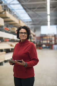 Thoughtful female customer holding digital tablet while standing in hardware store warehouse