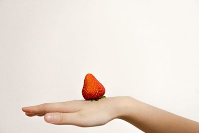 Close-up of hand holding strawberry over white background