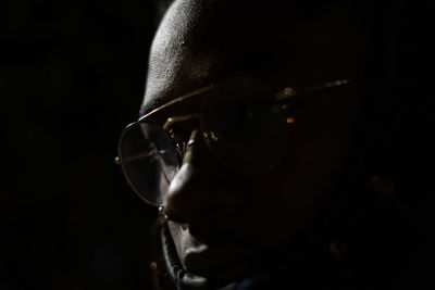 Close-up portrait of man wearing eyeglasses against black background