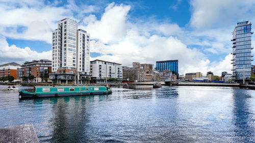 Boats in harbor by buildings against sky