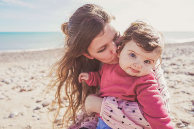 Mother kissing baby on beach against sky