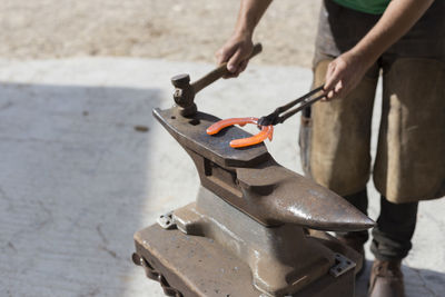 Unrecognisable farrier holding red hot horseshoe on an anvil